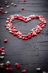Heart made with small candy hearts, pink, red, white colors, on dark background. Love, Valentine's day concept. Top view, copy space.