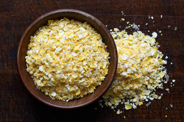 Dry flaked corn in brown wooden bowl isolated on dark wood.