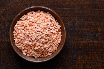 Dry red lentils in brown wooden bowl isolated on dark wood.