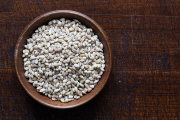 Dry pearl barley in brown wooden bowl isolated on dark wood.