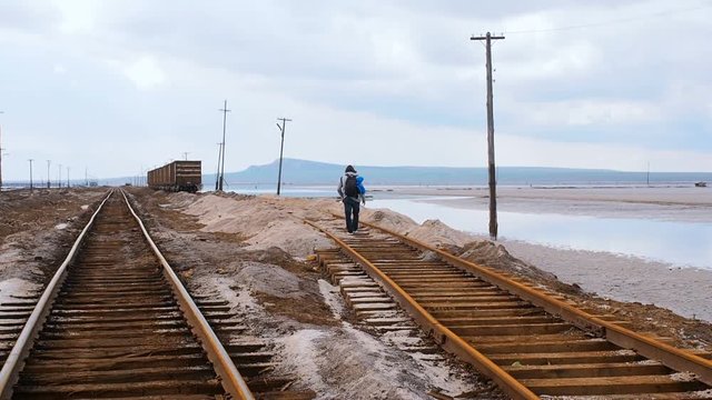 Man goes by rail. Tourist walking on cross ties to old wagons. Old rusty railroad through salt lake. Saline salt lake Baskunchak Astrakhan region Russia