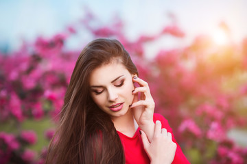 Spring touch. Happy beautiful young woman in red dress enjoy fresh pink flowers and sun light in blossom park at sunset.