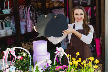 Attractive flower seller holding empty speech bubbles and looking at camera standing at floral store