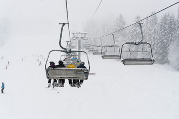 Mountasins ski resort landscape with pine trees. People on ski lift wearing yellow, blue, black...