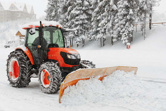 Red snowblower grader clears snow covered ski resort road in mountains or city street. Winter snowflake snowfall cold fog, mist weather. Horizontal, copy space.