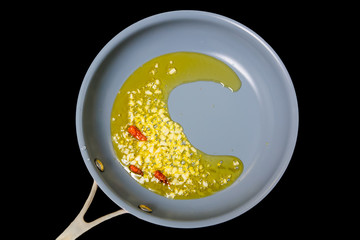 Garlic and small chili peppers are fried in oil in a frying pan.