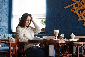 Sad girl sits at little table and looks downwards.