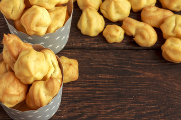 Sweet tasty eclairs or profiterole in gray paper cups with stars on wooden background. French dessert. Empty space for design text template.