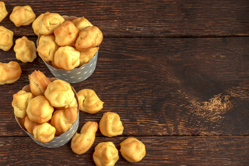 profiterole or sweet tasty eclairs in gray paper cups with stars on wooden background. French dessert. Empty space for design text template.