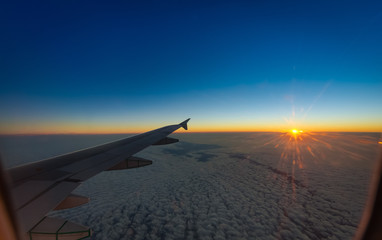 aircraft window view of wing with setting sun and deep blue sky and clouds below  (A320)