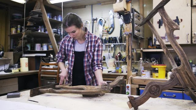 A young attractive carpenter is restoring the wood element of some furniture. A concept of a workshop. Locked down.