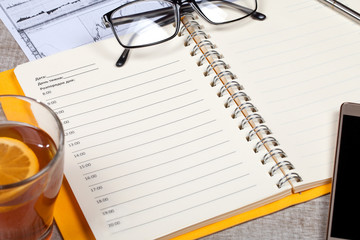 Top view of open notebook, glasses, a cup of tea, pen and smartphone on a wooden table
