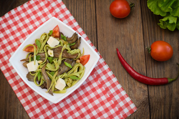 Plate of spaghetti dough with spinach and oyster mushrooms. Italian cuisine, Italian recipes. Wooden background. Top view. Close-up