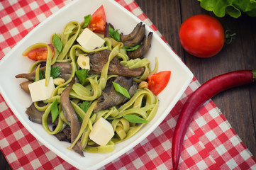 Plate of spaghetti dough with spinach and oyster mushrooms. Italian cuisine, Italian recipes. Wooden background. Top view. Close-up