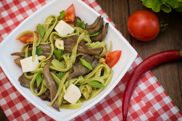 Plate of spaghetti dough with spinach and oyster mushrooms. Italian cuisine, Italian recipes. Wooden background. Top view. Close-up