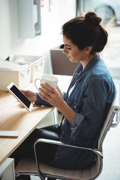 Businesswoman using digital tablet and holding coffee cup in office