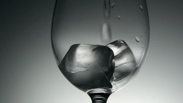 Close up of water being poured into glass with ice cubes, slow motion.