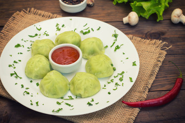 Georgian dumplings Khinkali of spinach dough with meat and tomato spicy sauce satsebeli. Wooden background. Top view. Close-up