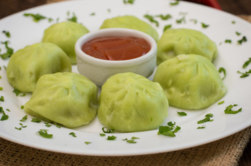 Georgian dumplings Khinkali of spinach dough with meat and tomato spicy sauce satsebeli. Wooden background. Top view. Close-up