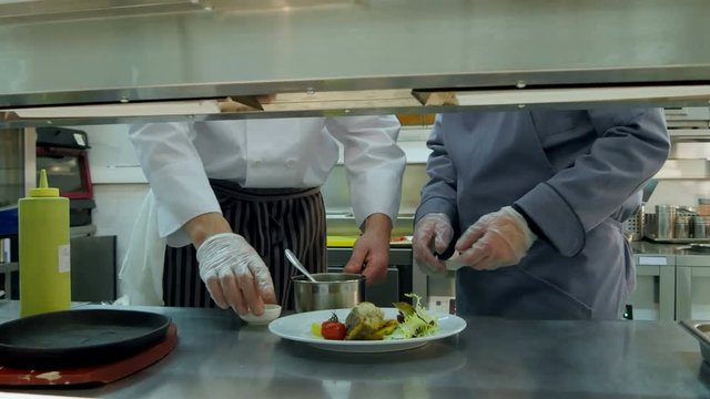 Chef teaching young trainee how to serve the sauce
