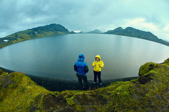 hikers on the Lake coast with mountain reflection at the rainy day, Iceland. Two hikers take pictures of the lake