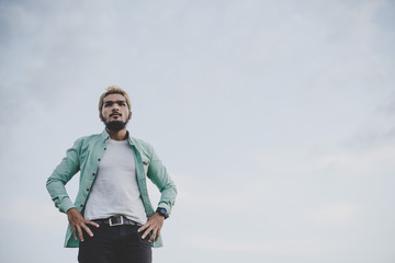 Young hipster man standing in the park with sky looking away.
