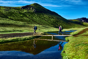 Travel to Iceland. Beautiful Icelandic landscape with hikers and bridge over creek, mountains, sky and clouds. Trekking in national park Landmannalaugar