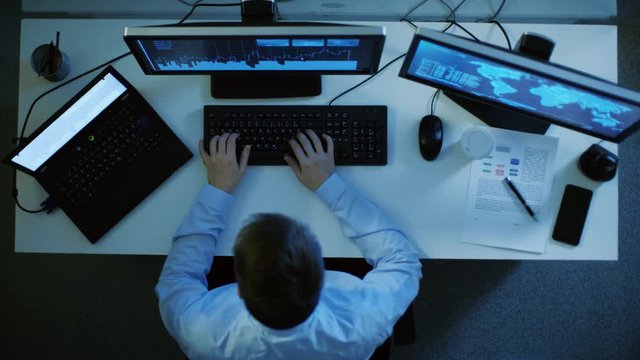 Top View of IT Specialist Working With International Servers and Internet Traffic. He Working on His Personal Computer and Laptop Simultaneously. Shot on RED EPIC-W 8K Helium Cinema Camera.