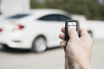Hand of man holding and push remote control of car and white car parking background technology...