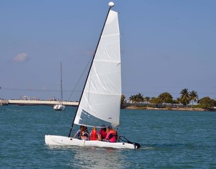 Naklejka premium Four teen agers and one adult enjoying a saturday afternoon cruise on a small sailing catamaran on the florida intra-coastal waterway near miami beach.