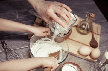 Little girl and her mother cook dough for home-made cupcakes. 