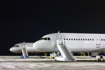The front part of the two aircraft with passenger boarding stairs at night winter airport apron