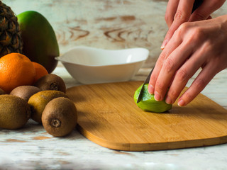 Woman cutting fruits on chopping board. Female hands cutting kiwi fruits close up