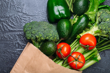 Food background of green vegetables broccoli romaine lettuce celery pepper zucchini tomatoes in shopping bag on black table Healthy lifestyle Top view Copy space