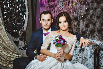 Wedding day. The bride and groom in a luxurious interior in lavender color. Wedding emotions. Beautiful bride and elegant groom at the ceremony.