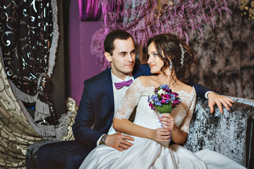 Wedding day. The bride and groom in a luxurious interior in lavender color. Wedding emotions. Beautiful bride and elegant groom at the ceremony.