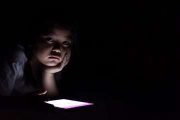 Kid with tablet sitting on bed and watching cartoons at night.