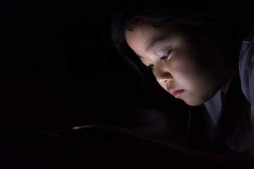 Kid with tablet sitting on bed and watching cartoons at night.