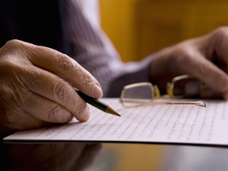 Close up of a hands of an old man, writing in a paper.