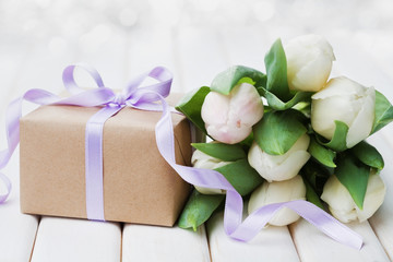 Spring tulip flowers and gift box with bow ribbon on white table. Greeting card for Birthday, Womens or Mothers Day.
