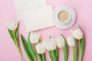 Coffee mug, paper card and spring tulip flowers for good morning on pink table from above in flat lay style. Breakfast on Mothers or Womens day.