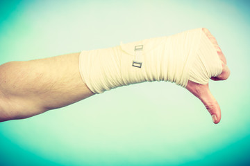Male bandaged hand with thumb down sign.