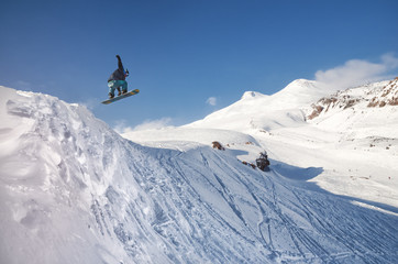 Stylish snowboarder with helmet and mask jumps from high snow slope