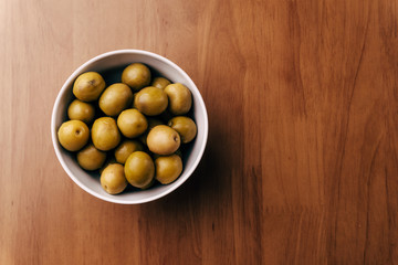 Fresh green olives in white bowl on wooden table background. Top view with copy 