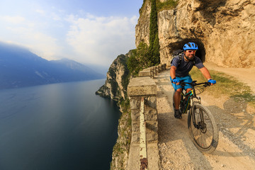 Mountain biking at sunrise man over Lake Garda on path Sentiero