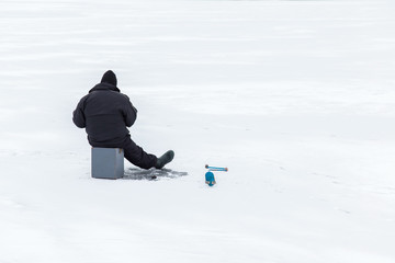 Fototapeta na wymiar Angler with equipment fishing on the lake ice in winter day. Fisherman.