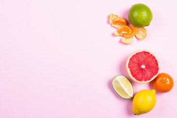 Several kinds of whole and cut citrus on a pink background