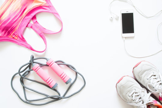 Flat lay of cellphone, pink sport bra, jump rope and sneaker on