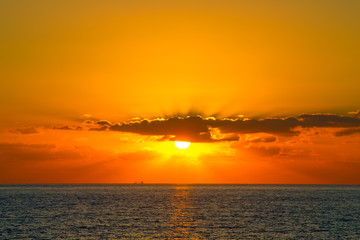 Obraz premium Orange sunset with rays shines through the clouds at Paphos coas