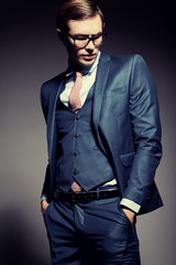 Obraz premium Young elegant handsome businessman male model in blue suit and fashionable glasses, posing in studio